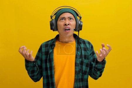 Genervter asiatischer Mann in Mütze und lässiger Kleidung ächzt vor Frustration, während er Kopfhörer trägt. Laute Musik oder Lärm werden impliziert. Vereinzelt auf gelbem Hintergrund.