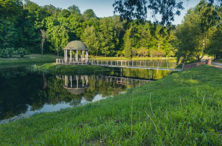 Foto de Una alcoba en el agua, un puente que conduce a ella, hierba verde y un lago en primer plano. Foto de alta calidad - Imagen libre de derechos