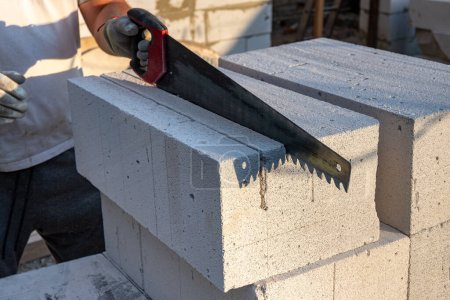 Téléchargez les photos : Le processus de sciage des blocs de béton aéré avec une scie à main. Construction de briques de béton aéré, blocs. Photo de haute qualité - en image libre de droit