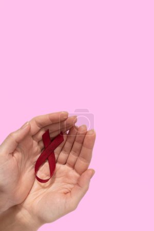 Woman holding red ribbon as symbol of World Cancer Day, on pink background, cancer awareness sign. High quality photo