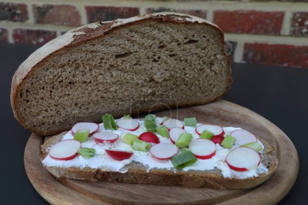 Photo for Half a loaf of stone baked bread with a traditional Pajottenland sandwich of a slice of bread spread with fresh cheese sprinkled with radishes and spring onions - Royalty Free Image