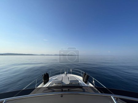 Photo for Bow of a private yacht in the calm mediterranean waters sailing towards a distant shore - Royalty Free Image