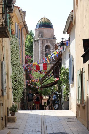 Photo for Narrow French street with festive flags and the bell tower of the black penitent brotherhood chapel in the background - Royalty Free Image