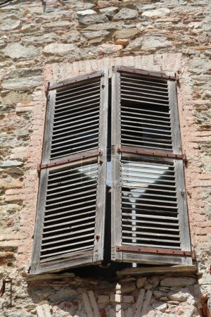 Téléchargez les photos : Fenêtre dans un mur de pierre avec de vieux volets en bois altérés presque fermés pour fermer le soleil chaud d'été - en image libre de droit