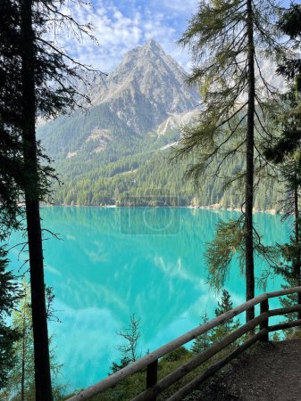 emerald green water of Lake Antholz and high Dolomiti mountains seen through the coniferous trees of the surrounding forest 