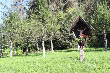 Wooden wayside cross in a green orchard in the Alps