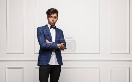 Photo for Self assured young male in smart casual clothes crossing arms and looking at camera while standing against white wall - Royalty Free Image