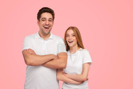 Photo for Cheerful young man and woman in white t shirts crossing arms and looking at camera with smile against pink background - Royalty Free Image