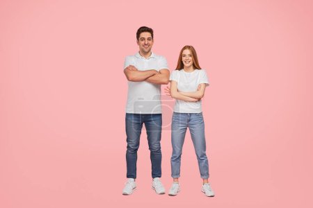 Photo for Full body glad young man and woman in similar outfits crossing arms and looking at camera with smile while standing against pink background together - Royalty Free Image