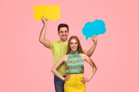 Photo for Happy man smiling and demonstrating bright speech bubbles while standing behind girlfriend in stylish colorful clothes against pink background - Royalty Free Image