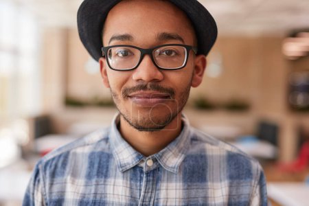 Photo for Smart black man in checkered shirt with glasses and hat looking at camera on blurred background of workspace - Royalty Free Image