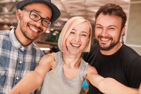 Photo for Merry blond woman smiling and taking selfie with multiracial boyfriends on weekend day - Royalty Free Image