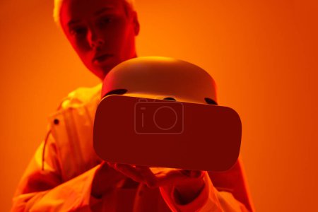 Téléchargez les photos : Joueuse futuriste démontrant des lunettes VR modernes sous éclairage au néon orange - en image libre de droit