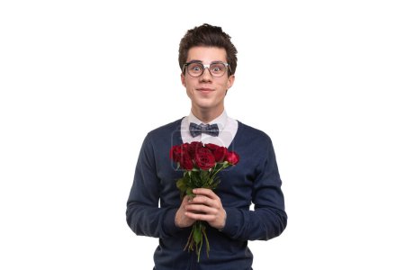 Foto de Feliz joven hombre en ropa casual inteligente y gafas con racimo de rosas rojas sonriendo y mirando a la cámara durante la fecha contra el fondo blanco - Imagen libre de derechos