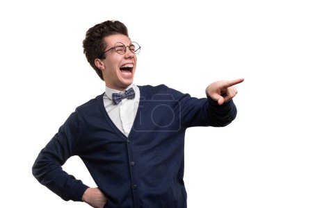 Photo for Funny young man in smart casual clothes and glasses holding hand on waist and pointing away while laughing with closed eyes against white background - Royalty Free Image