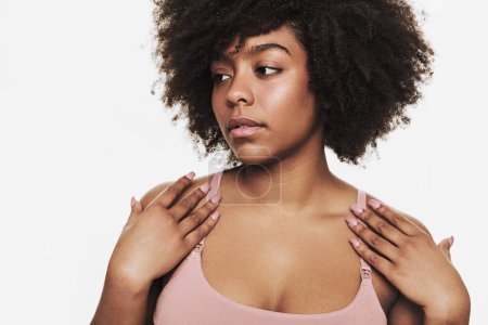 Photo for African American woman with curly hair touching straps of pink bra and looking away against white background - Royalty Free Image
