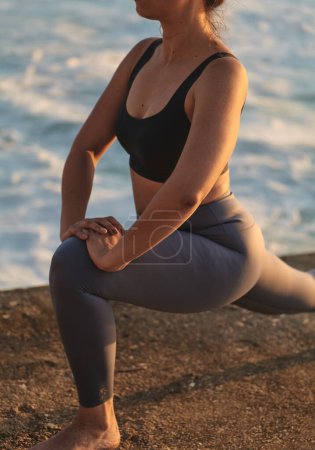 Photo for Side view of unrecognizable barefoot female in sportswear stretching before practicing yoga at oceanside - Royalty Free Image