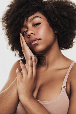 Téléchargez les photos : Young calm African American female model with dark curly hair and perfect skin in underwear touching face and looking at camera against white background - en image libre de droit