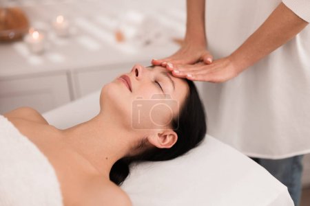 Téléchargez les photos : From above of crop unrecognizable therapist massaging face of relaxed young female client, lying on table with closed eyes during acupressure treatment in light salon - en image libre de droit