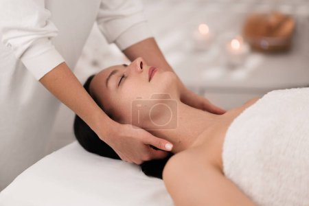 Téléchargez les photos : High angle of crop unrecognizable masseuse massaging head and neck of young female client with dark hair, relaxing on couch with closed eyes during treatment - en image libre de droit