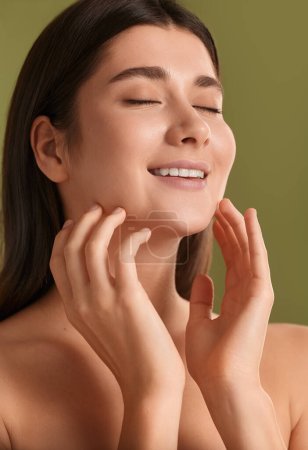 Téléchargez les photos : Closeup face of Cheerful young female with closed eyes touching clean skin and enjoying fresh skincare routine against green background - en image libre de droit
