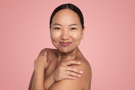 Téléchargez les photos : Positive young asian female with bare shoulders looking at camera on pink background in studio - en image libre de droit