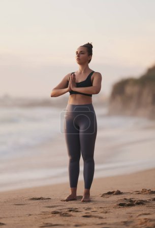 Photo for Full length of peaceful young barefooted female with dark hair in top and leggings, standing on sandy beach in Mountain with Prayer Hands asana while practicing yoga near ocean - Royalty Free Image