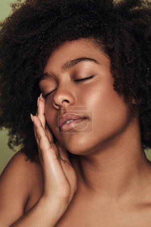 Photo for Self assured young ethnic female millennial with curly Afro hair and perfect skin touching face with closed eyes, during beauty routine - Royalty Free Image