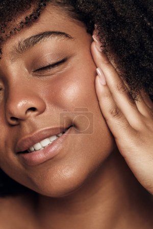 Téléchargez les photos : Closeup of crop young African American female model with perfect skin and curly dark hair, smiling with closed eyes while applying moisturizing cream on face - en image libre de droit
