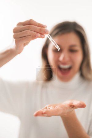 Téléchargez les photos : Mise au point douce de la jeune femme joyeuse avec pipette versant sérum hydratant sur la main tout en faisant la procédure de soins de la peau - en image libre de droit