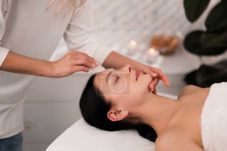 Photo for Crop anonymous female beautician massaging clients forehead with gua sha during skin care procedure in beauty salon - Royalty Free Image