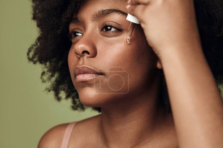 Photo for Closeup beauty Portrait of young African American female with Afro hairstyle, using serum product as skin care routine on face - Royalty Free Image