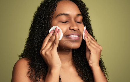 Foto de Mujer afroamericana optimista con el pelo rizado sonriendo cara de limpieza de maquillaje mientras está de pie sobre fondo verde - Imagen libre de derechos