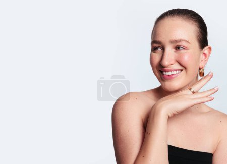 Photo for Positive young female model with perfect natural skin and bare shoulders standing against white background looking away - Royalty Free Image