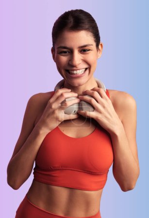 Photo for Glad Hispanic lady in crop top looking at camera while standing against violet background and touching headphones on neck - Royalty Free Image