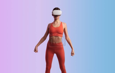 Téléchargez les photos : Corps complet de la jeune femme sportive mince en VR lunettes debout avec fond de vêtements de sport à la mode en studio - en image libre de droit