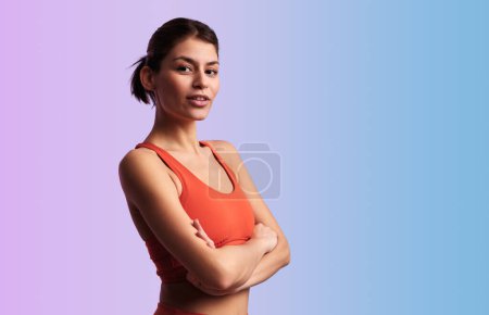 Photo for Content Hispanic female in red crop top standing on gradient backdrop and crossing arms while looking at camera - Royalty Free Image