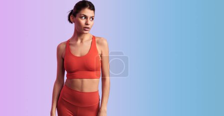 Photo for Fit Hispanic female model in red activewear looking away attentively while standing on gradient backdrop - Royalty Free Image