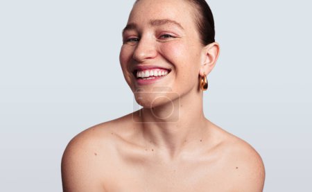 Téléchargez les photos : Portrait de modèle féminin heureux avec peau propre du visage regardant la caméra et souriant tout en faisant la routine de soins de la peau du matin sur fond blanc - en image libre de droit