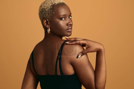 Téléchargez les photos : Vue arrière du jeune modèle féminin africain aux cheveux blonds afro et à la peau parfaite regardant par-dessus l'épaule sur fond orange - en image libre de droit