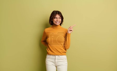 Photo for Happy young female in casual outfit with hand behind back pointing away at empty space against yellow background - Royalty Free Image