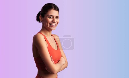 Photo for Positive young athletic female in red sports top standing with crossed hands against gradient background looking at camera - Royalty Free Image