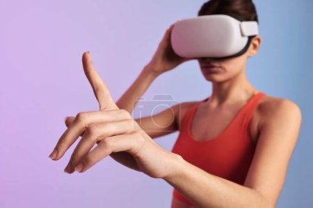 Téléchargez les photos : Mise au point douce de jeunes lunettes VR féminines ajustables tout en touchant un objet invisible avec un doigt explorant le cyberespace sur fond de dégradé - en image libre de droit