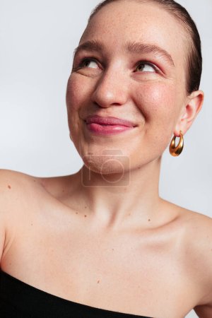 Foto de Retrato de mujer joven atractiva con el pelo corto y pecas mirando hacia otro lado contra el fondo blanco - Imagen libre de derechos