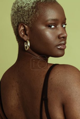 Téléchargez les photos : Jeune modèle féminin afro-américain auto-assuré avec des cheveux blonds courts portant un soutien-gorge regardant la caméra sur fond vert - en image libre de droit