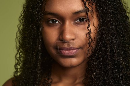 Téléchargez les photos : Gros plan du visage de la jeune femme africaine à la peau propre parfaite, représentant la beauté naturelle, après la routine du matin, en regardant la caméra en studio sur fond vert - en image libre de droit