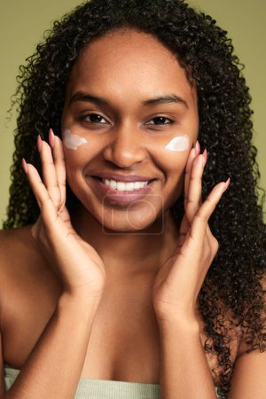 Téléchargez les photos : Jeune femme afro-américaine au visage crème et regardant la caméra sur fond vert - en image libre de droit