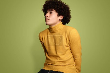 Foto de Modelo masculino casual con peinado afro con cuello alto amarillo de moda y mirando hacia otro lado en el fondo verde del estudio - Imagen libre de derechos