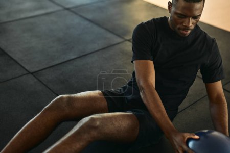 Photo for High angle of crop African American male athlete sitting on mat doing Russian twists with medicine ball during workout at gym - Royalty Free Image