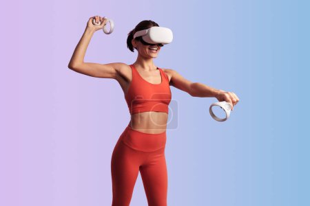 Téléchargez les photos : Femme anonyme excitée portant des lunettes VR à l'aide de manettes de jeu tout en jouant au tennis en ligne dans le jeu virtuel sur fond de dégradé - en image libre de droit